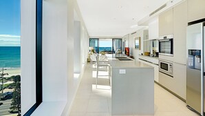 A modern kitchen with a large island, built-in appliances, and a view of the ocean. - Soul Private Apartments (Surfers Paradise)