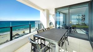 A balcony with a view of the beach and ocean, a table with chairs, and a glass door leading to an interior space. - Soul Private Apartments (Surfers Paradise)