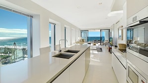 A modern kitchen with a large island, a dining area, and a view of the ocean. - Soul Private Apartments (Surfers Paradise)