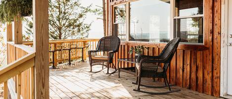 A wooden deck with wicker chairs and a table, overlooking a scenic landscape.
