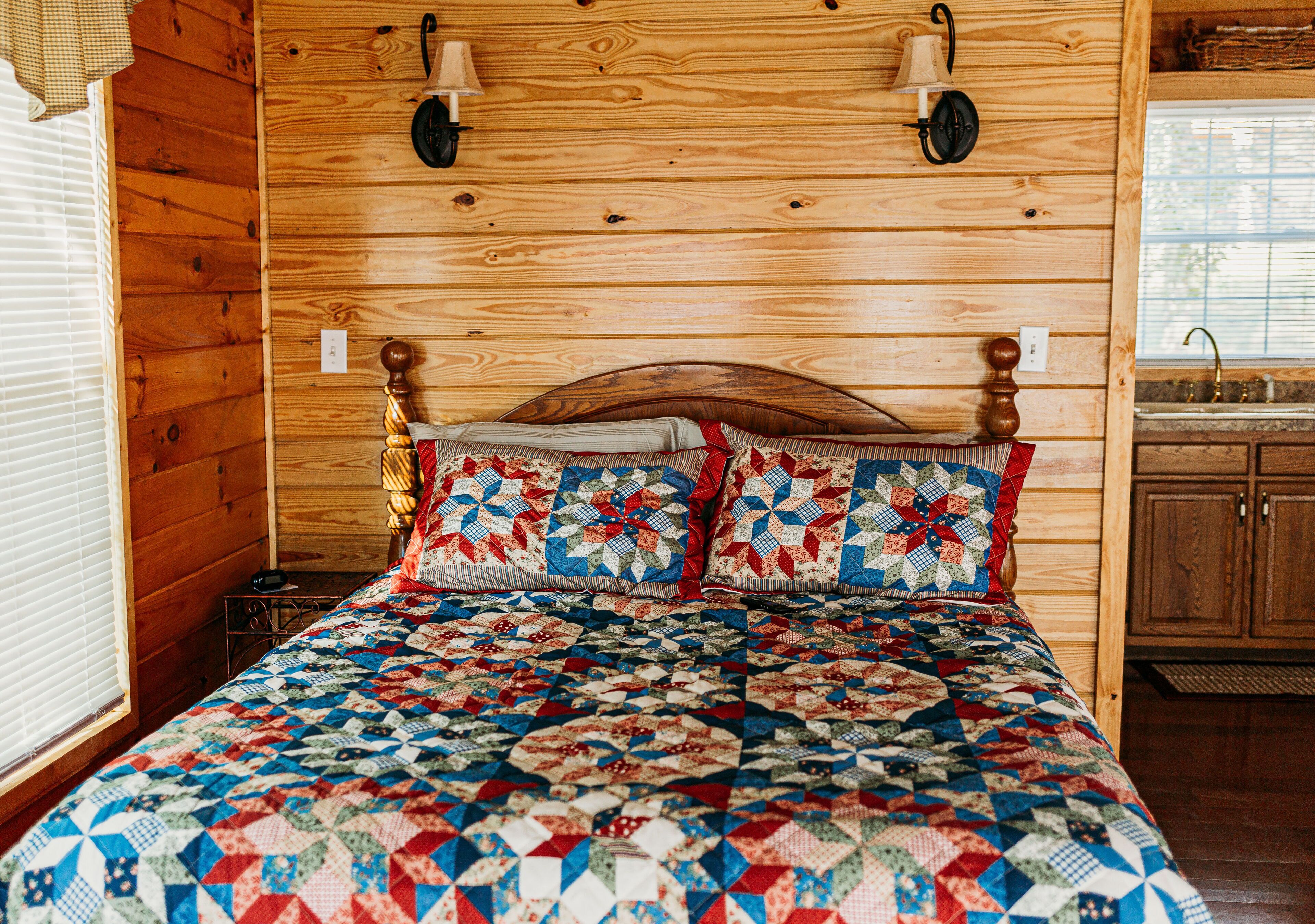 A wooden-paneled bedroom with a quilted bedspread, a wooden headboard, and a small bedside table with a lamp.