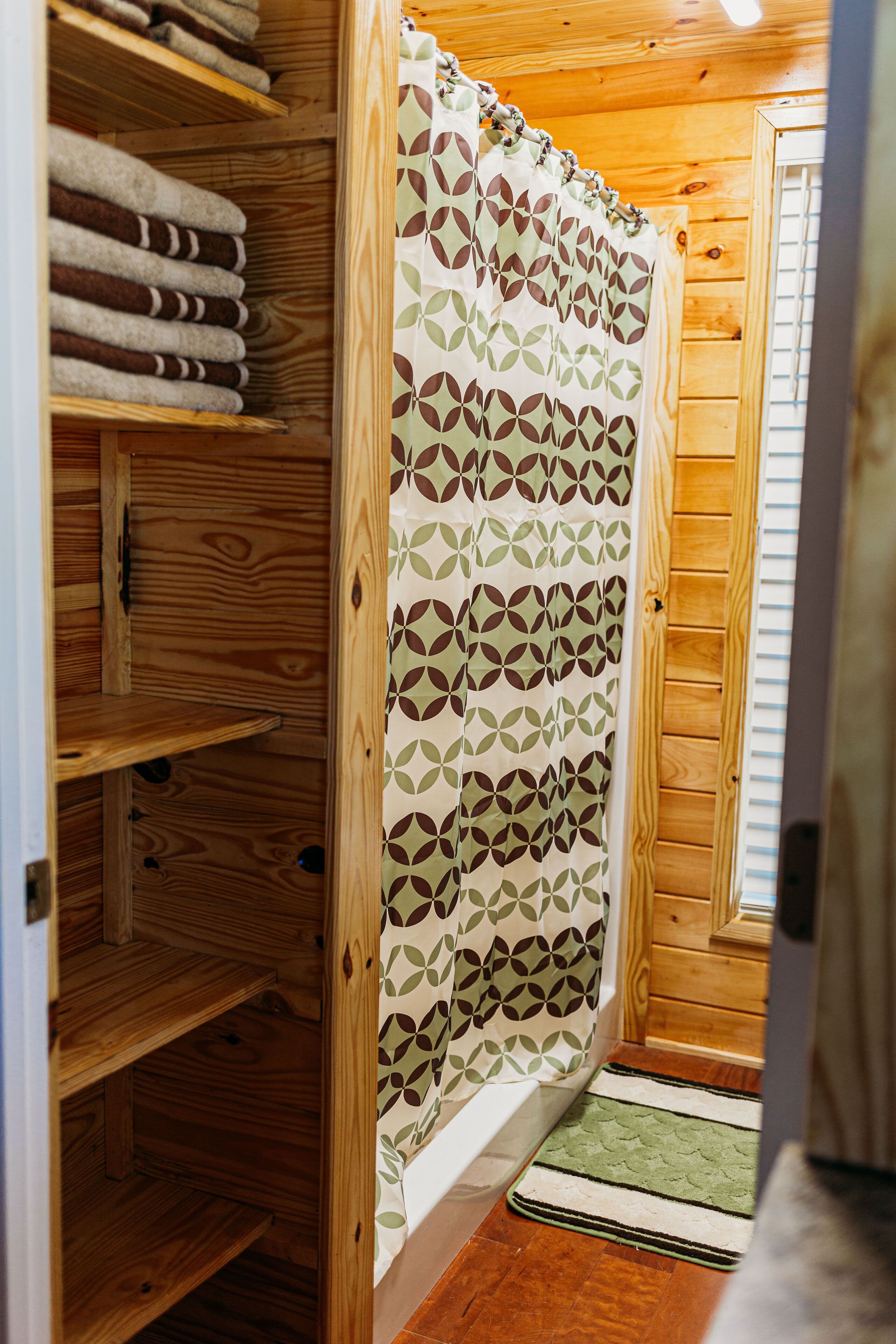 A wooden interior with a shower curtain, wooden shelves, and a green mat.