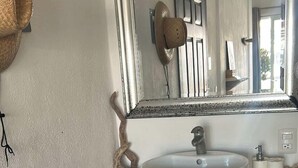 Une salle de bain avec un lavabo rond, des meubles en bois, un miroir et un petit objet décoratif accroché au mur.