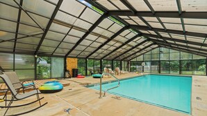 An indoor swimming pool with a glass ceiling, lounge chairs, and a poolside area. - MOUNTAIN JOY COTTAGES #5 - STARS AND STRIPES (Maggie Valley)