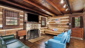 A log cabin interior with a stone fireplace, leather sofas, and a television. - MOUNTAIN JOY COTTAGES #5 - STARS AND STRIPES (Maggie Valley)