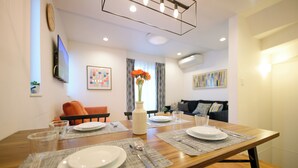 A dining area with a wooden table set for four, including plates, cutlery, and glasses. There is a vase with flowers on the table, and the room has a modern design with a flat-screen TV mounted on the wall. - Sangen-jaya House-O (Tokyo)