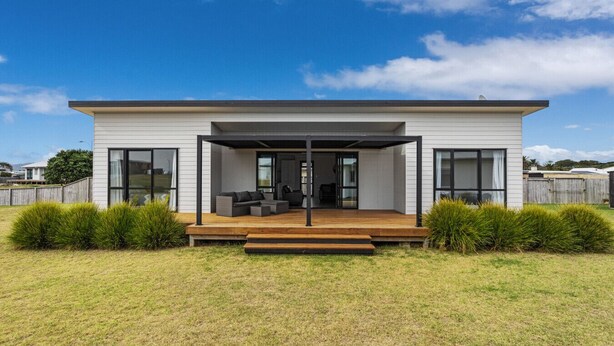 Une maison moderne dotée d’un patio couvert, de grandes fenêtres et d’une cour gazonnée.