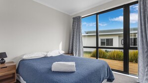 Une chambre avec un grand lit, une table de chevet, une fenêtre avec des rideaux et une vue sur un bâtiment à l’extérieur.