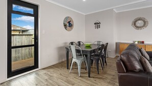 Un coin repas avec une table et des chaises, un plancher en bois, une porte noire et une vue sur un jardin.