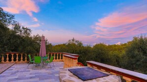 An outdoor patio with stone flooring, green chairs, a table, and a pink umbrella.