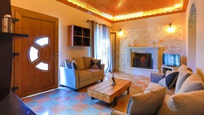 A cozy living room with a wooden ceiling, a stone fireplace, and a sofa set.