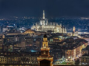 Uma paisagem urbana noturna com edifícios iluminados e uma catedral imponente ao fundo.