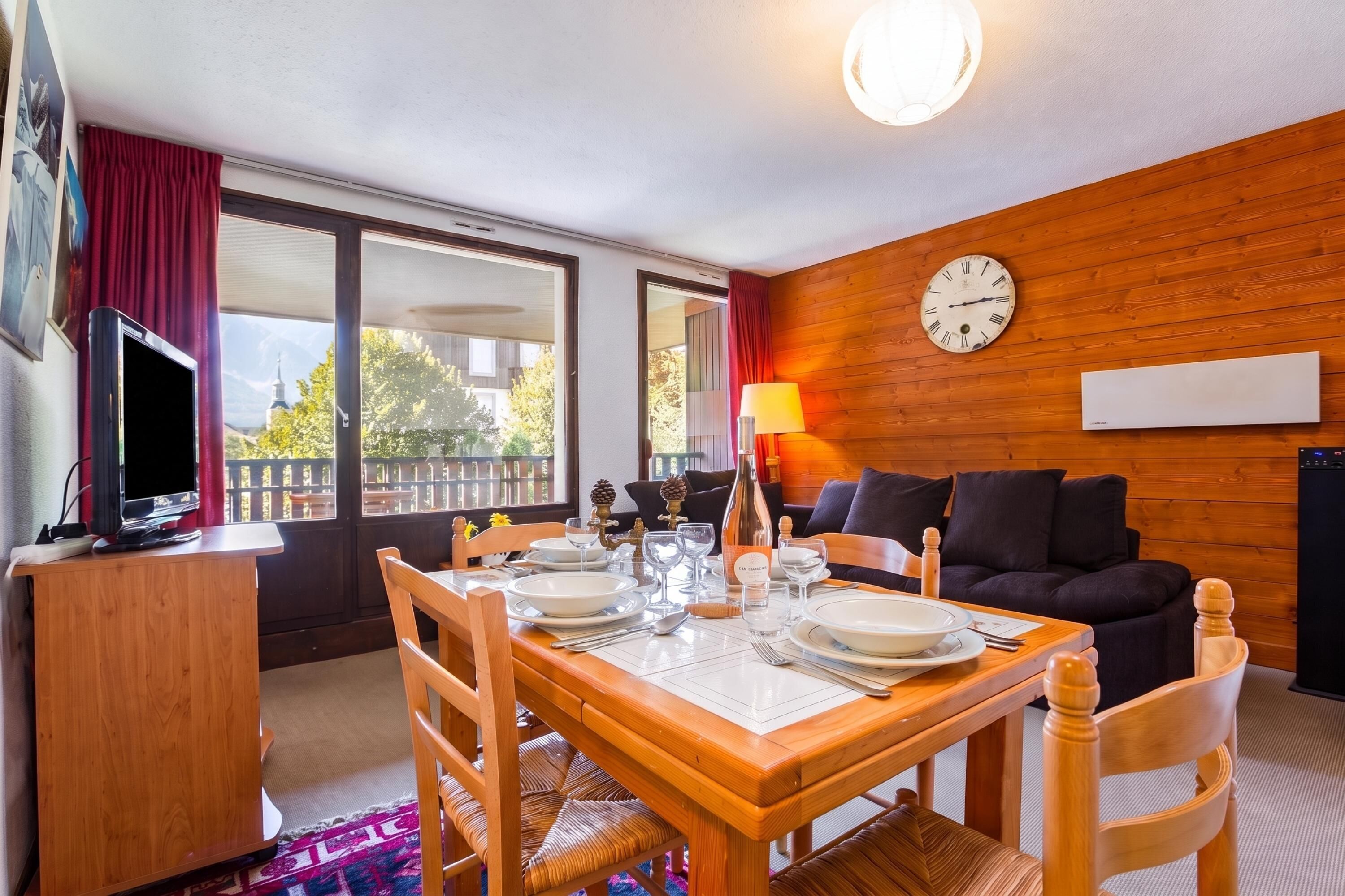 Una habitación con una mesa de comedor lista para cuatro personas, un sofá, un televisor y un reloj en la pared.