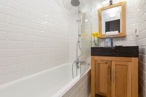 Une salle de bain moderne avec des carreaux de céramique blancs rectangulaires, une douche à parois de verre, un meuble-lavabo en bois avec un plan de travail noir et un miroir au-dessus du lavabo.