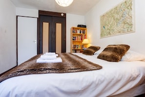 Quarto com uma cama grande, uma estante de livros, um mapa na parede e uma porta.