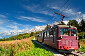Un tramway d’époque circulant sur des rails, avec une chaîne de montagnes en arrière-plan.
