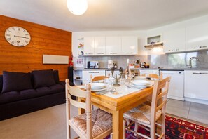 A modern living space with a dining area, kitchen, and a wooden wall with a clock.
