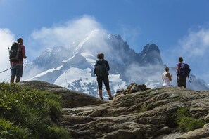 Un groupe de personnes se tient au sommet d’une montagne rocheuse, avec des montagnes enneigées en arrière-plan.