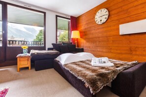 Una camera d'albergo con un letto, un divano, un tavolino, una lampada e una sveglia appesa al muro.
