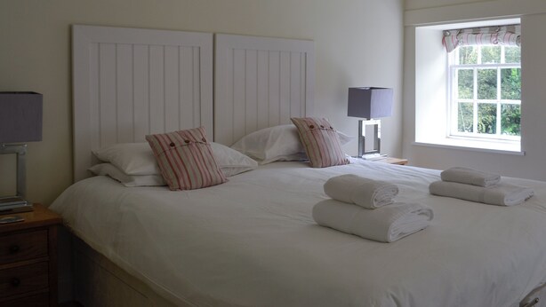 A neatly made bed with white linens and striped pillows, a bedside lamp, and a window with curtains.
