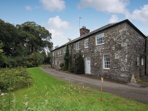 A stone building with a gravel driveway, surrounded by greenery and trees.