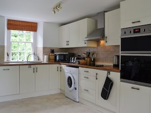 A kitchen with white cabinets, a washing machine, a microwave, and an oven.