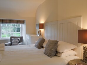 A bedroom with a bed, bedside table, lamp, chair, and a window with curtains.
