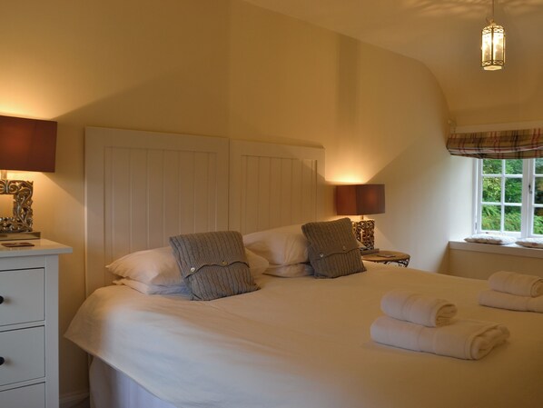 A bedroom with a large bed, bedside tables with lamps, a window with a view, and a ceiling light fixture.