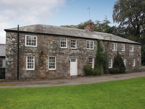 A stone building with multiple windows and a door, surrounded by a grassy area.