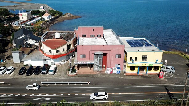 A coastal hotel with a parking lot, a road with vehicles, and a view of the sea. - Tabist Izumi Yusen Shukuhaku Center (Izumi)