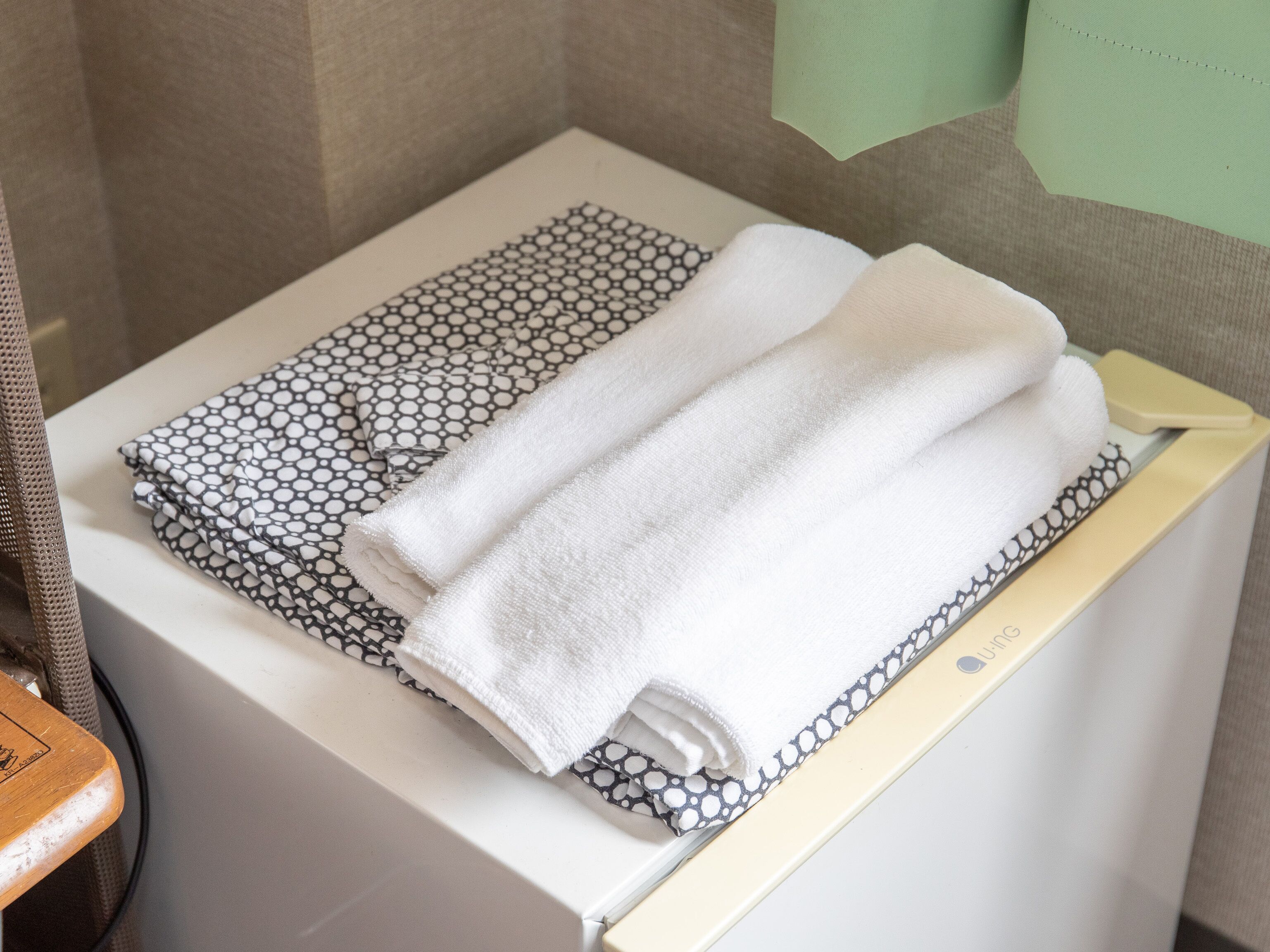 A bathroom with a white towel and a patterned towel on a white shelf.