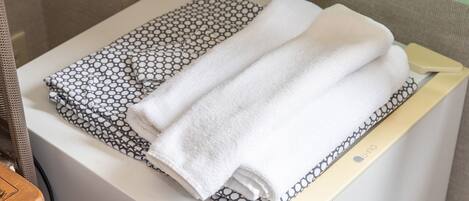 A bathroom with a white towel and a patterned towel on a white shelf.