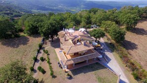 A two-story house with a tiled roof, surrounded by trees and a hilly landscape.