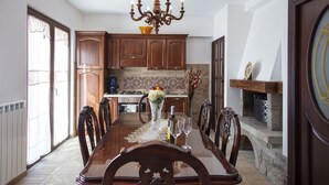 A dining room with a wooden table, chairs, a chandelier, and a kitchen in the background.