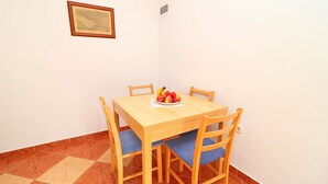 Ein Essbereich mit einem Holztisch und Stühlen, einer kleinen Obstschale auf dem Tisch und einem gerahmten Bild an der Wand.