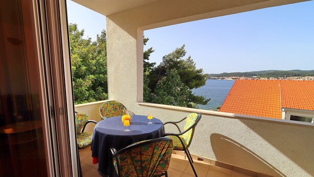 Ein Balkon mit Tisch und Stühlen, Blick auf das Meer und ein Ziegeldach im Hintergrund.
