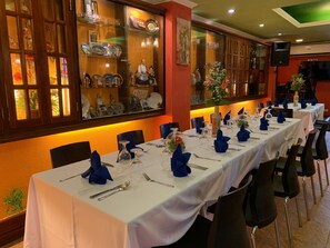 A restaurant with a long dining table set with blue napkins, silverware, and glassware.
