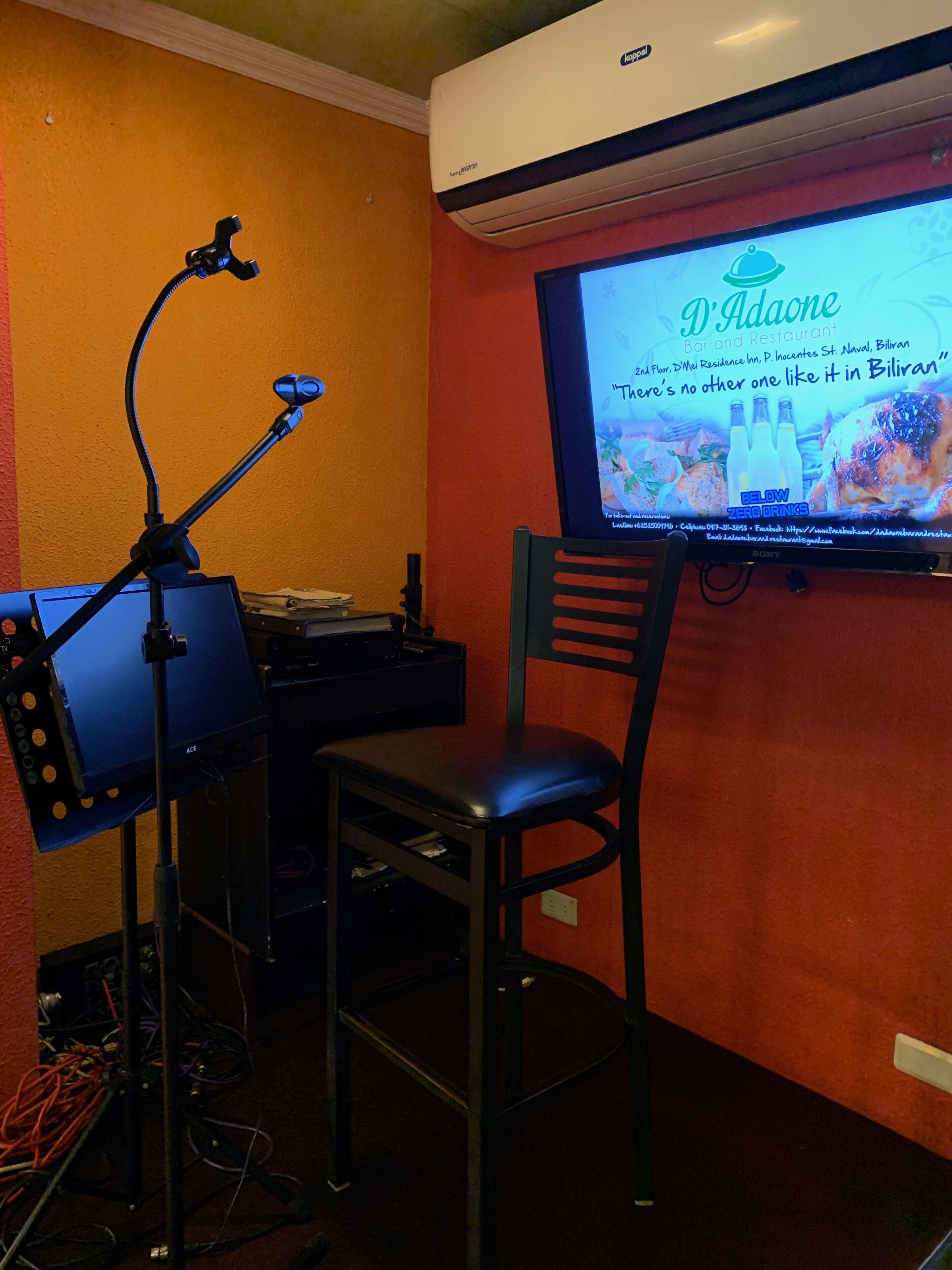 A room with a television displaying a restaurant advertisement, a desk with a computer, and a chair.