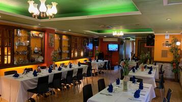 A restaurant with multiple tables set for dining, a bar area, and a television screen.