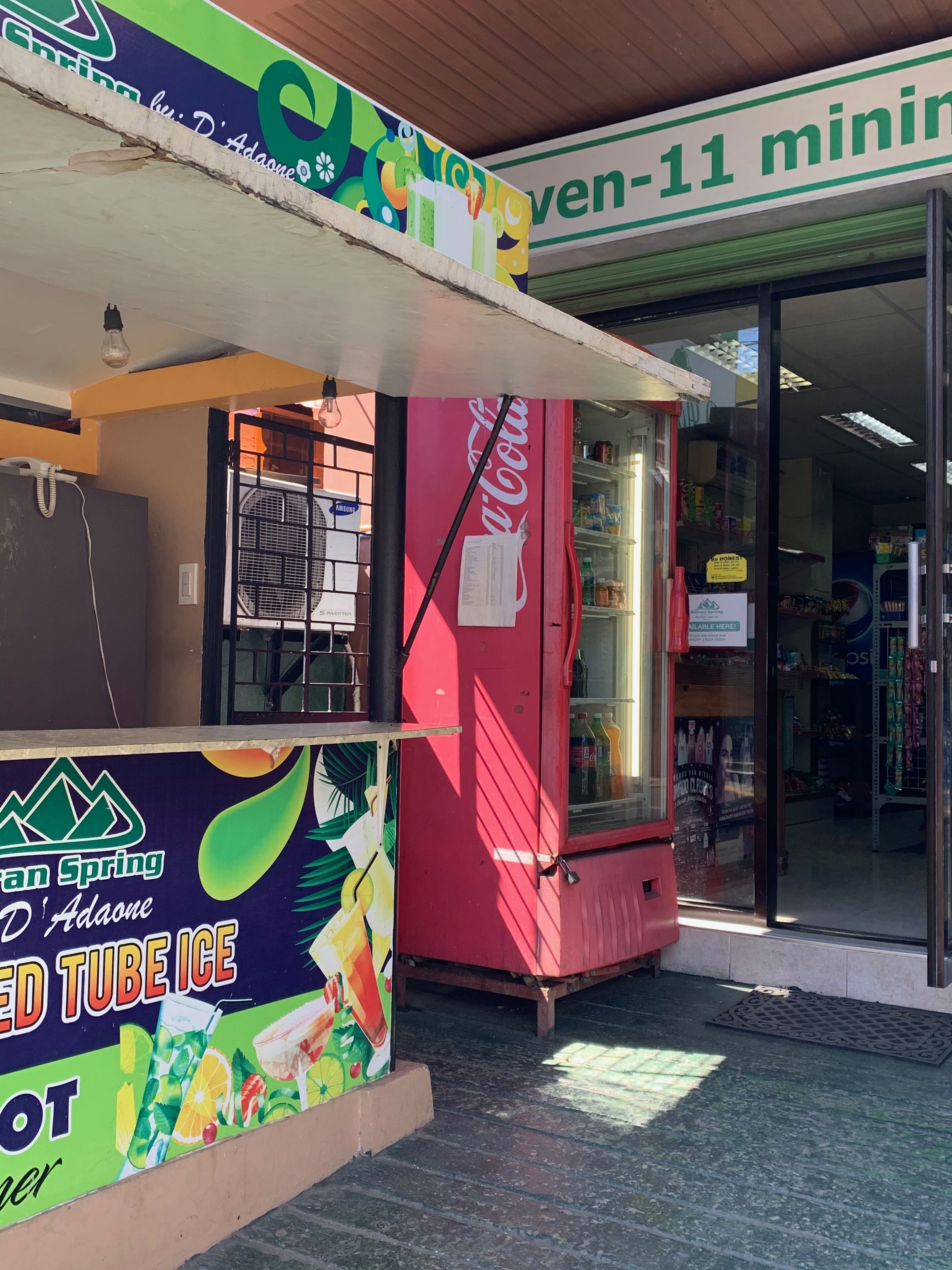 A colorful ice cream cart with a Coca-Cola logo, a Samsung refrigerator, and a sign for 'Green Spring Adaone'.