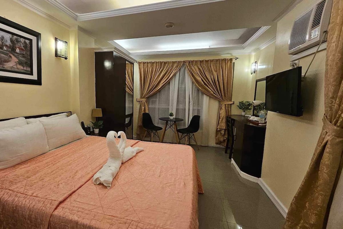 A hotel room with a large bed, a desk, a chair, a TV, and a painting on the wall.