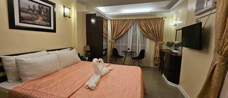 Een hotelkamer met een groot bed, een bureau, een stoel, een televisie en een schilderij aan de muur.