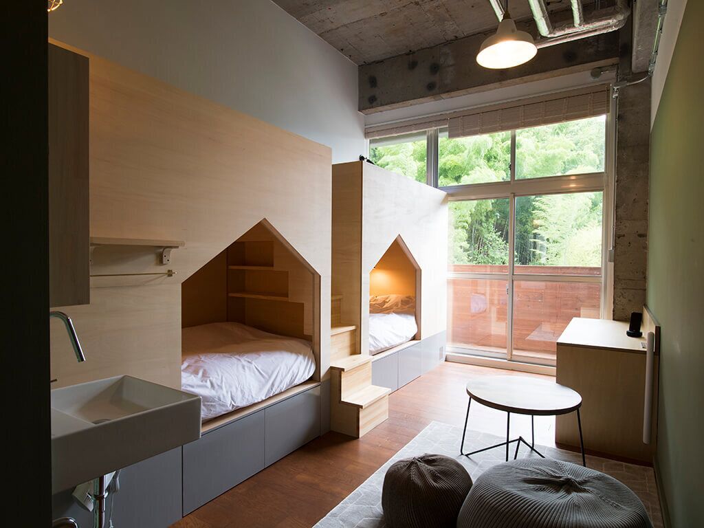A compact bedroom with built-in storage, a bedside table, and a window with a view of greenery.