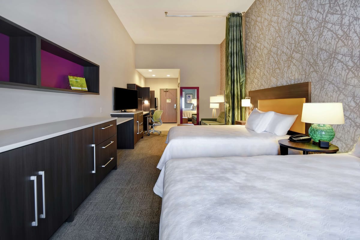 A hotel room with two beds, a desk with a computer, a television, and a bathroom visible through an open door.