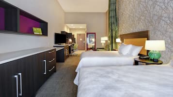 A hotel room with two beds, a desk with a computer, a television, and a bathroom visible through an open door.