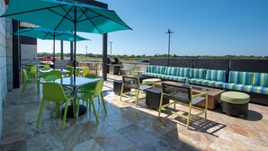 An outdoor patio with green chairs, a table, and a sofa under a blue umbrella. - Home2 Suites by Hilton Wichita Northeast (Wichita)