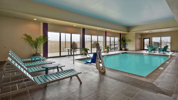 An indoor swimming pool with lounge chairs and tables, large windows, and potted plants. - Home2 Suites by Hilton Wichita Northeast (Wichita)