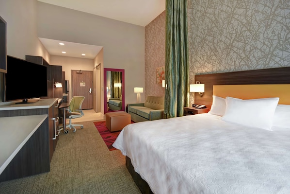 A hotel room with a bed, desk, TV, and seating area.