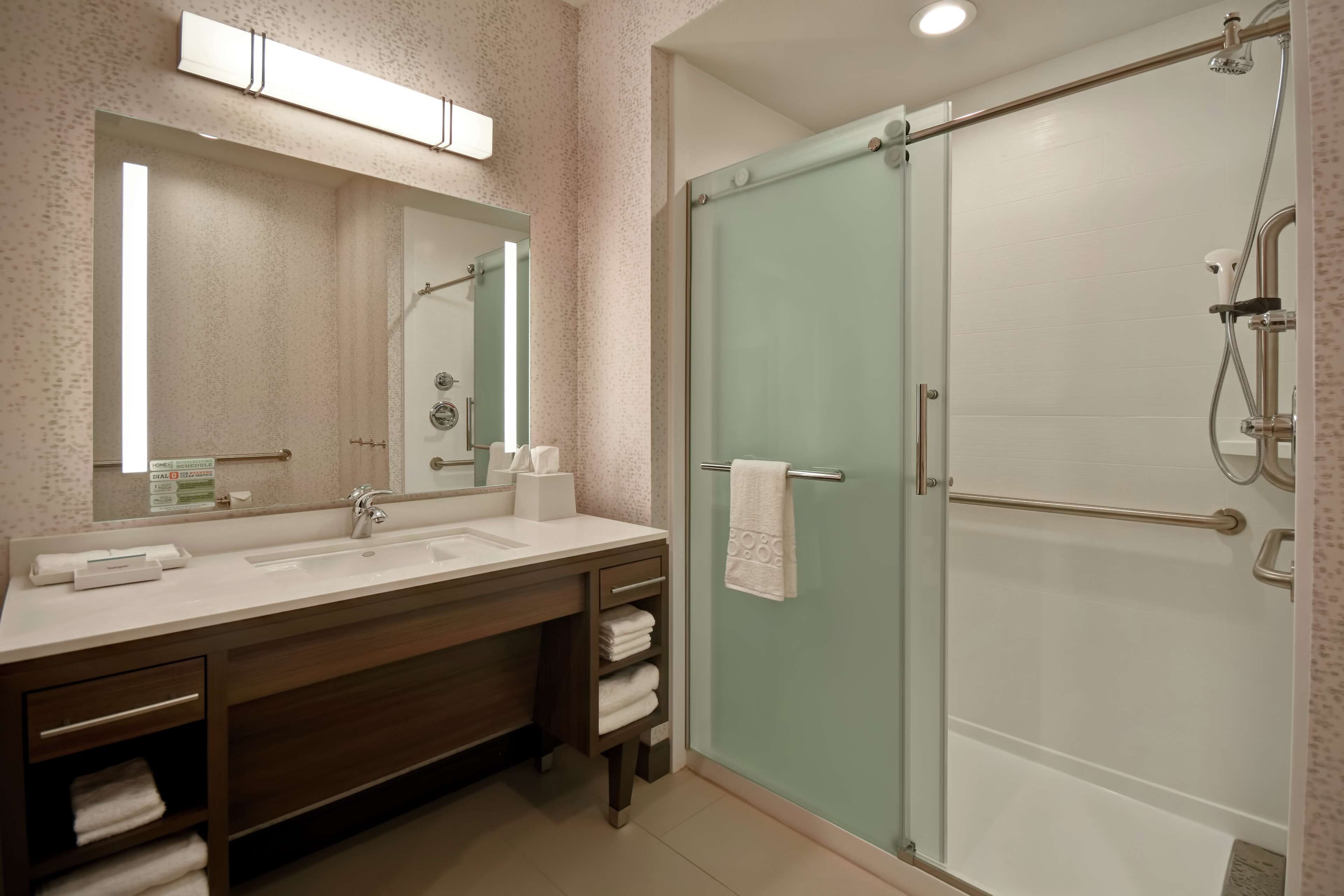 Een moderne badkamer met een douchecabine van glas, een grote spiegel en een wastafel met een handdoekrek.