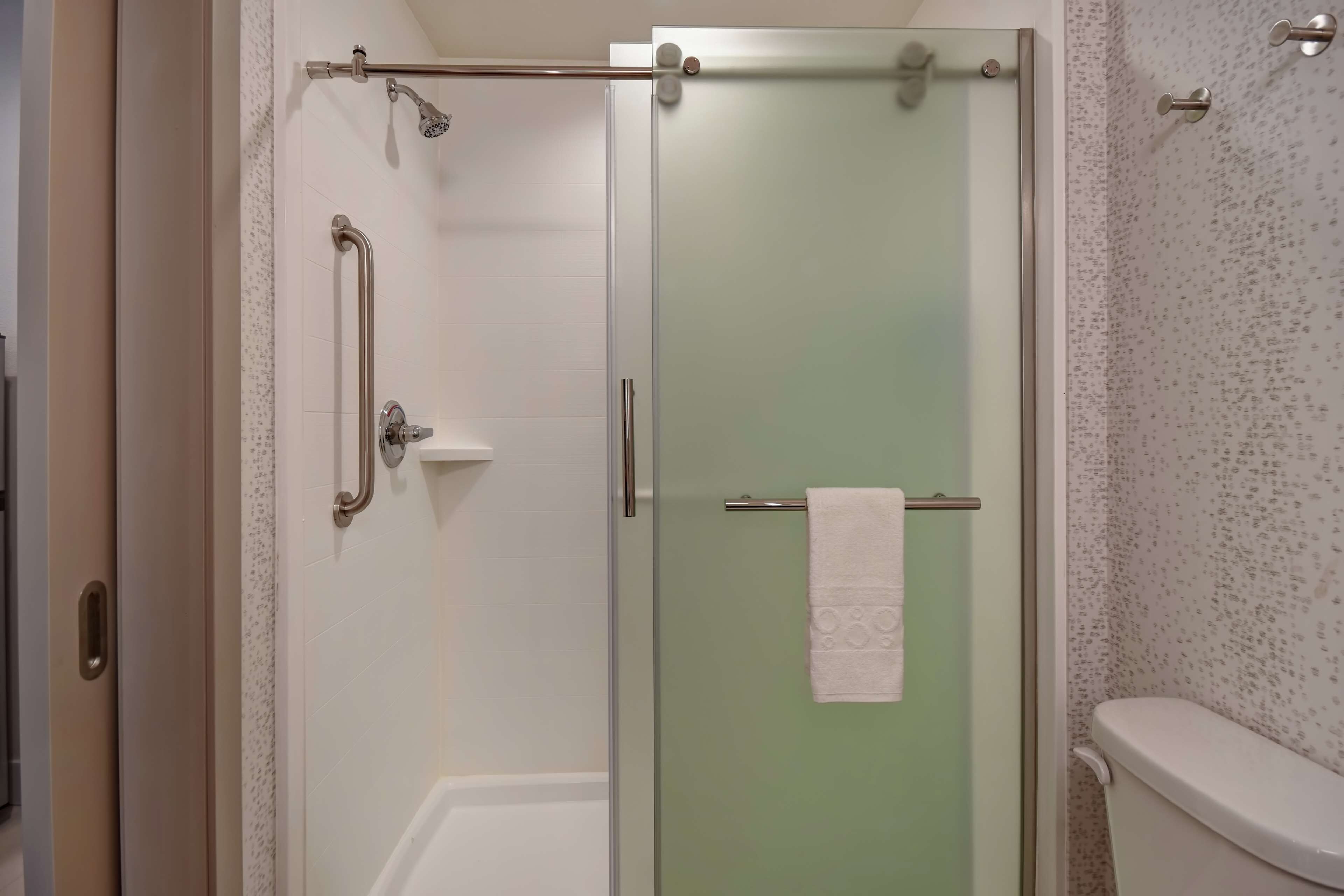 A glass-enclosed shower with a handrail, a towel rack with a towel, and a toilet with a speckled wall.